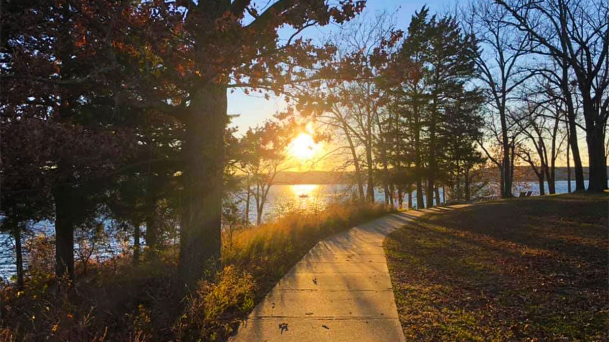 pathway surrounded by greenery with view of lake and sun shining at Table Rock Lakeshore Trail in Branson, Missouri, USA